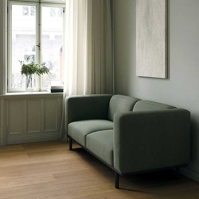 Andersen Furniture A1 Sofa mit grünem Stoffbezug Kvadrat Fiord 961 und schwarz lackiertem Gestell aus massiver Eiche, entworfen von byKATO, in einem hellen Wohnraum mit Holzboden.