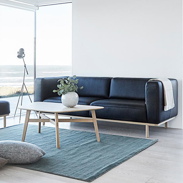 Andersen Furniture A1 Sofa als 3-Sitzer mit schwarzem Lederbezug und hellem Eichengestell, entworfen von byKATO, in einem modernen Wohnzimmer mit Couchtisch und Meerblick.