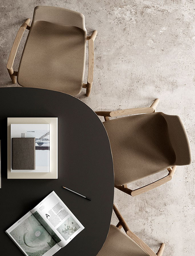 Modernes Restaurant- oder Café-Interieur mit schwarzen Tischen, grünen Holzstühlen (Modell Andersen AC2) und einer gepolsterten Sitzbank im Hintergrund. Auf den Tischen stehen Gläser und Besteck, im Fensterbereich Pflanzen.