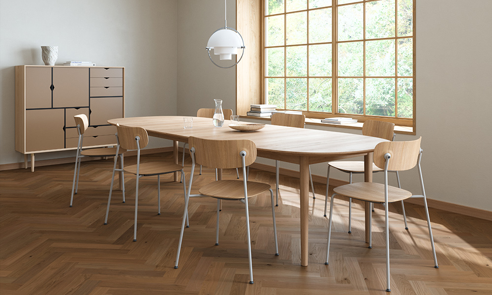 Der Andersen Furniture Classic Esstisch aus massiver Eiche mit Seifenfinish und eleganter C-Kante bildet den Mittelpunkt eines modernen skandinavischen Esszimmers. Der ausziehbare Tisch mit Ansteckplatten bietet großzügig Platz für sechs Personen und harmoniert mit Holzstühlen auf weißem Metallgestell. Große Fenster, Parkettboden und ein minimalistisches Sideboard unterstreichen das zeitlose nordische Design und schaffen eine helle, einladende Wohnatmosphäre.