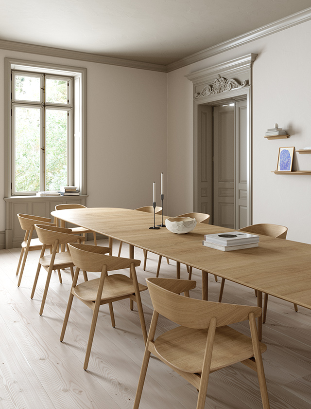 Ein großzügiger Essbereich mit dem Andersen Furniture Classic Esstisch aus massiver Eiche und acht passenden AC2 Esszimmerstühlen. Das helle skandinavische Interieur mit Holzboden, großen Fenstern und minimalistischer Einrichtung unterstreicht die natürliche Holzmaserung und das zeitlose nordische Möbeldesign. Der ausziehbare Esstisch eignet sich ideal für Familien und gesellige Runden.