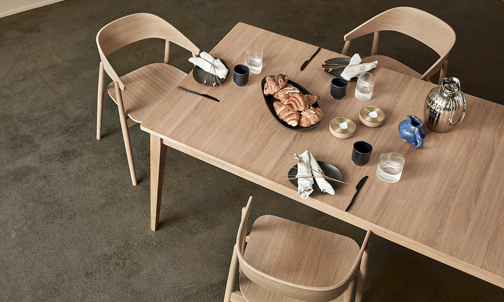 Andersen Furniture T10 Ausziehtisch aus Eiche in 95 × 200 cm, gedeckt mit Geschirr und Croissants, kombiniert mit AC2 Stühlen aus Eiche.