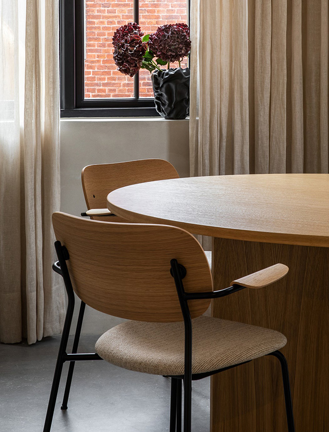 Der Stuhl steht auf einem schlichten, hellgrauen Boden vor einem grün-grauen Schrank mit dezenten Metallgriffen. Das minimalistische Interieur hebt die hochwertige Verarbeitung und das zeitlose Design des Möbelstücks hervor.