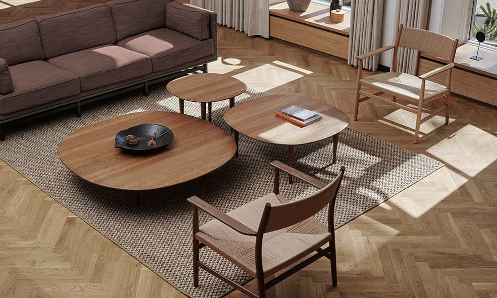 Wohnszene mit mehreren Brdr. Krüger Jari Low Tables aus Eiche in unterschiedlichen Größen und Höhen. Die runden und organisch geformten Tische sind als harmonisches Cluster vor einem Sofa arrangiert und zeigen die vielseitigen Kombinationsmöglichkeiten der Jari Beistelltische.