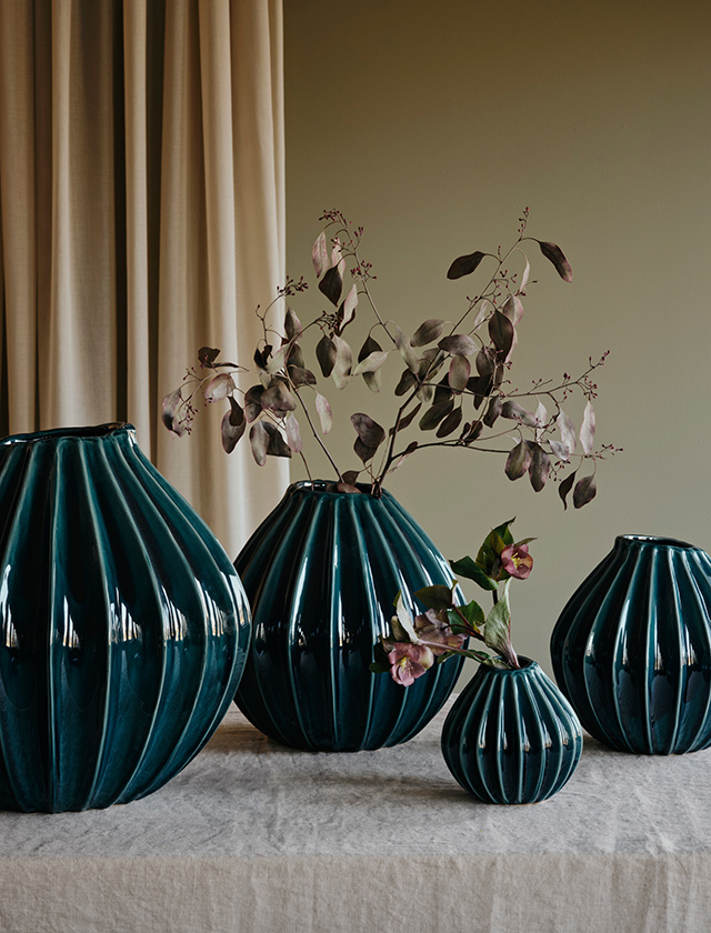 Broste Copenhagen Wide Vasen-Serie in Teal, einem tiefen Petrol- und Petroleumton – vier gerippte Keramikvasen in unterschiedlichen Größen, teilweise mit Blumen und Zweigen dekoriert.