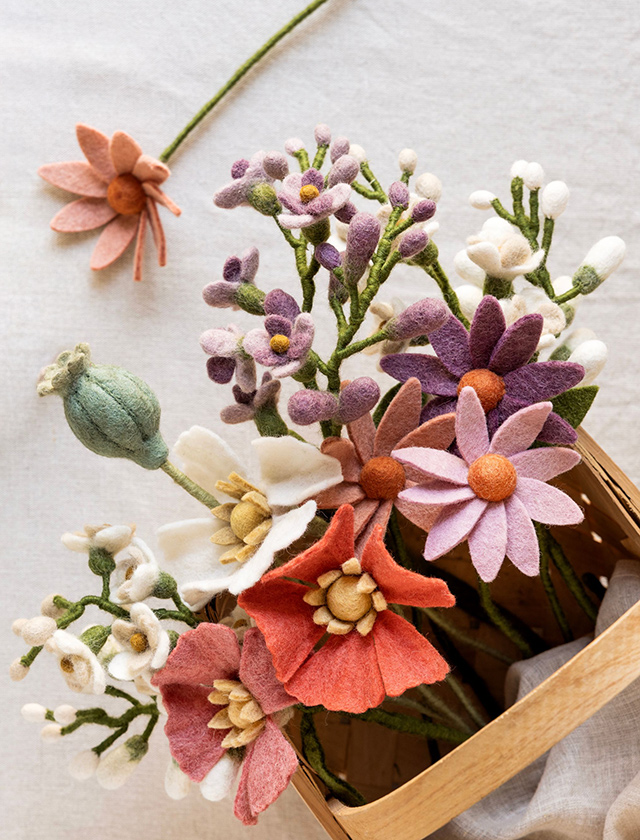 Bunter Strauß aus Gry & Sif Sommerblumen aus Wollfilz mit Mohnblumen, Kosmeen, weißen Blüten und grüner Mohnkapsel, dekorativ in einem Holzkorb arrangiert.