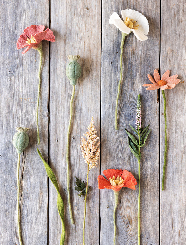 Verschiedene Gry & Sif Filzblumen mit roten und weißen Mohnblumen, grünen Mohnkapseln und weiteren Wiesenblumen auf hellem Holzhintergrund.