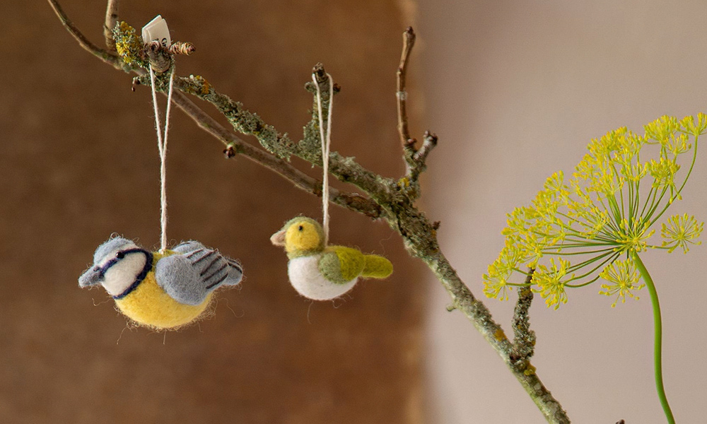 Handgefilzte Vögel von Gry & Sif – Blaumeise und kleiner Vogel aus Schurwolle als dekorative Filzanhänger an einem Zweig.