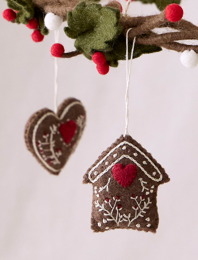 Handgefilzte Lebkuchenanhänger von Gry & Sif aus braunem Filz mit roten Herzen und weißen Stickdetails als Weihnachtsbaumschmuck.