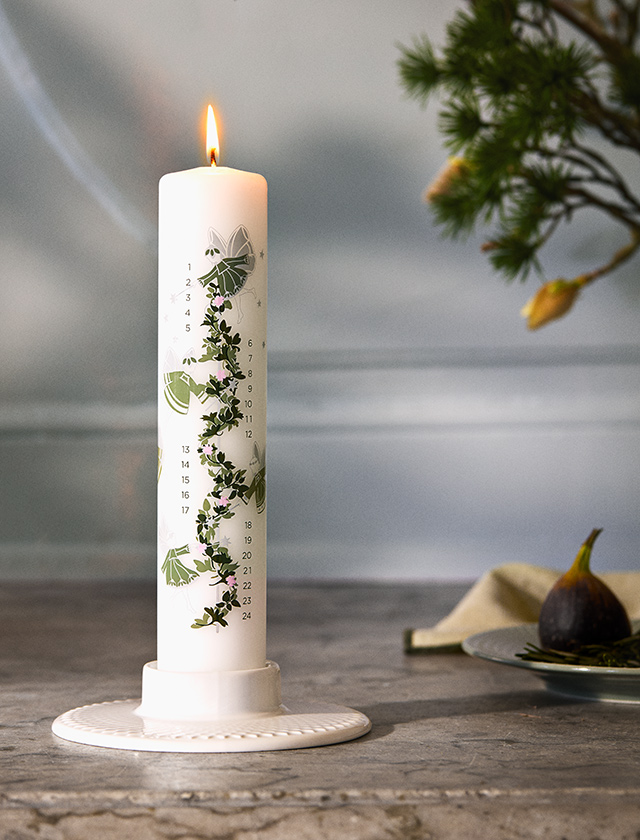 Holmegaard Christmas Kalenderkerze 2026 von Jette Frölich mit grünen Weihnachtsmotiven und Adventszahlen 1 bis 24, stimmungsvoll brennend auf einem Kerzenteller dekoriert.