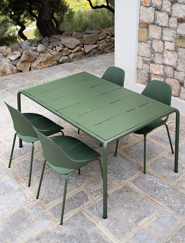 Modernen AVANTI Gartentisch in der Farbe Olive Green von HOUE, kombiniert mit vier passenden FALK Gartenstühlen in derselben Farbe. Die Szene spielt sich auf einer sonnigen Steinterrasse mit Natursteinboden ab, eingerahmt von einer Natursteinmauer und mediterranem Garten. Der AVANTI Tisch besticht durch sein minimalistisches, modulares Design mit klaren Linien und schmalen Schlitzen in der Tischplatte, die sowohl funktional als auch dekorativ sind. Die schräg platzierten Tischbeine an den Ecken maximieren die Beinfreiheit und die nutzbare Fläche. Das hochwertige pulverbeschichtete Stahlgestell sorgt für Stabilität und ist wetterfest – ideal für den Einsatz im Außenbereich. Der Tisch lässt sich durch Erweiterungselemente flexibel an verschiedene Sitzgruppen anpassen – vom kleinen Balkon bis zur großen Gartentafel. Design und Funktionalität treffen hier auf Nachhaltigkeit und erschwinglichen Luxus.