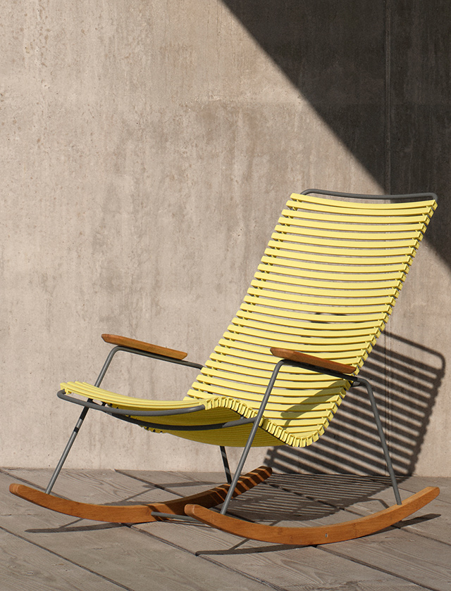 HOUE Click Schaukelstuhl in Lemon Zest vor einer Betonwand auf einer sonnigen Outdoor-Terrasse