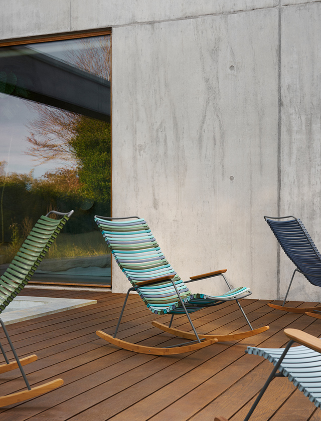 Mehrere HOUE Click Schaukelstühle in verschiedenen Farben auf einer Holzterrasse vor moderner Betonfassade