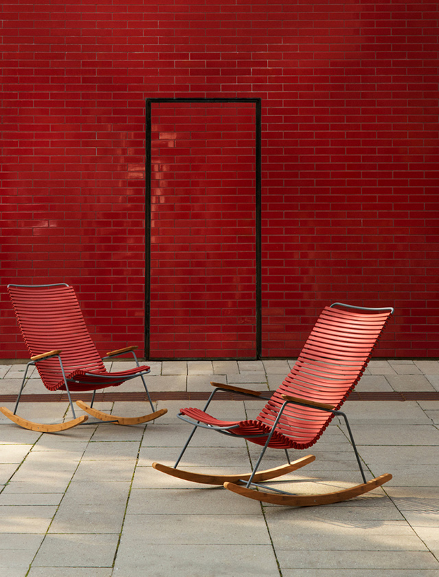 Zwei HOUE Click Schaukelstühle in Paprika auf einer Terrasse vor einer roten Wand