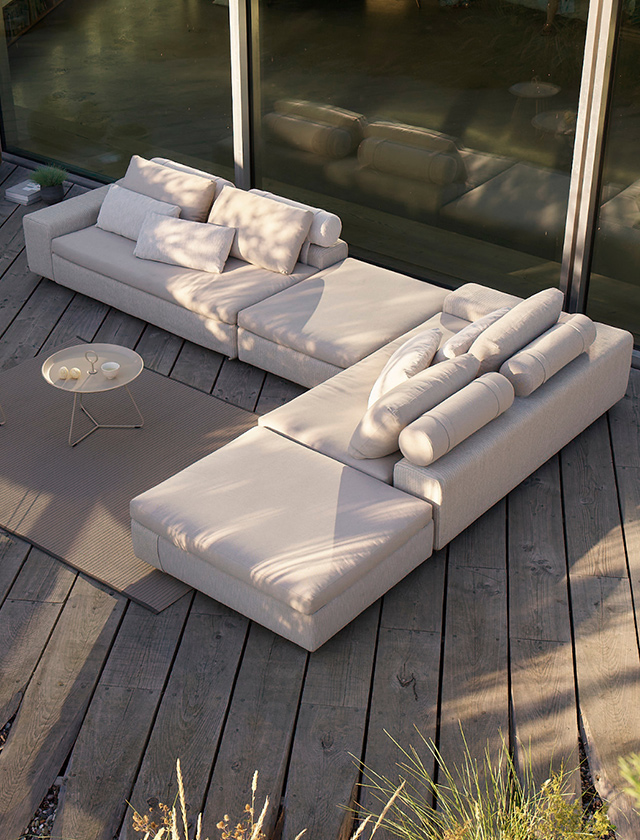 Helles modulares Outdoor-Lounge-Sofa der Serie HOUE DRIFT auf einer Holzterrasse vor einer großen Glasfront, mit weichen Polstern und entspanntem Premium-Look.