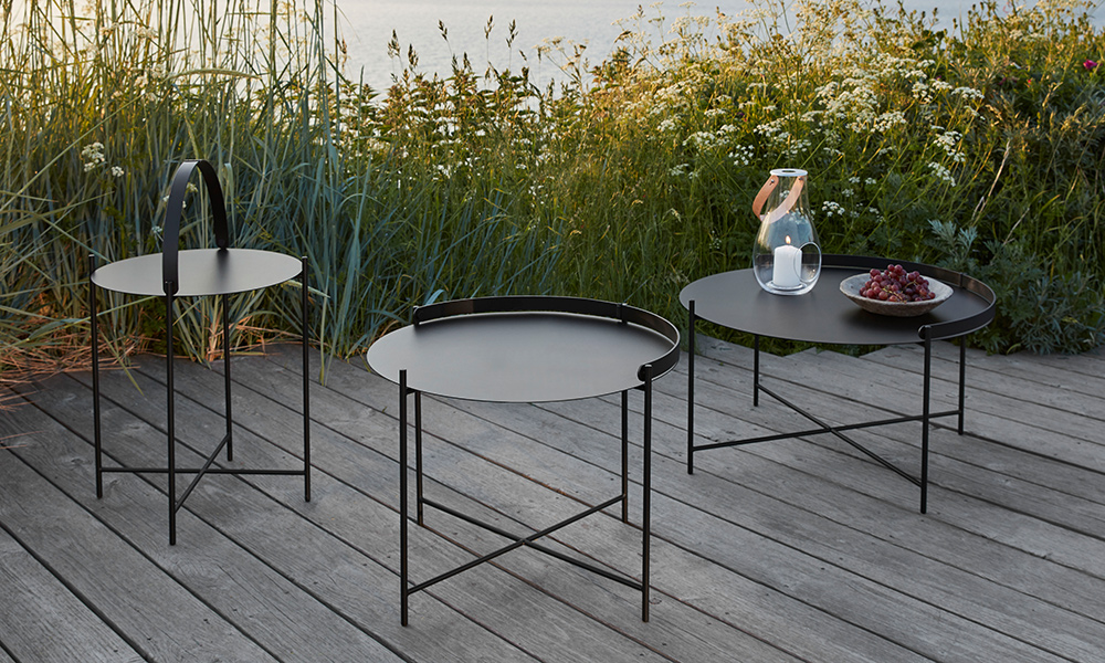Mitten in der Natur, auf einer Holzterrasse am Wasser, entfalten die EDGE Beistelltische von HOUE ihre volle Wirkung. In elegantem Schwarz und in drei abgestuften Größen präsentiert sich das minimalistische Tisch-Set als stilvoller Blickfang – funktional, zeitlos und perfekt für den Outdoorbereich.