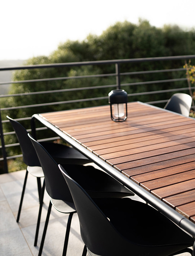 Hoch über der Landschaft, auf einer modernen Terrasse mit Fernblick, schafft dieses Ensemble aus dem AVANTI Infinity Tisch und FALK Gartenstühlen von HOUE eine elegante und zugleich naturnahe Atmosphäre. Der große, modulare Tisch begeistert mit seiner Tischplatte aus edler Thermoesche – langlebig, warm in der Haptik und von natürlicher Schönheit. Das schwarze Gestell aus pulverbeschichtetem Aluminium verleiht dem Tisch eine klare, minimalistische Linie und sorgt für maximale Stabilität im Outdoor-Einsatz.