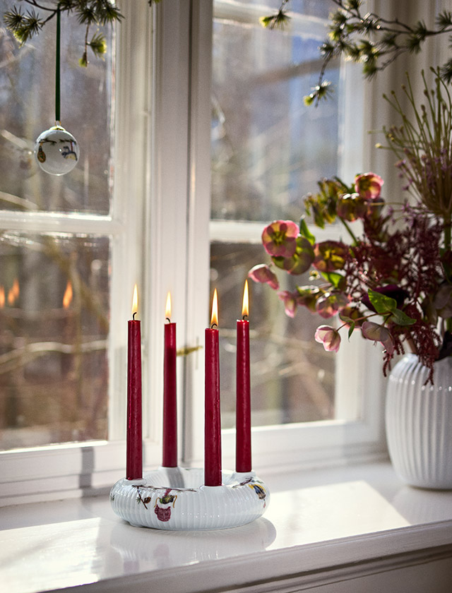Kähler Design Hammershøi Jul Adventskranz aus weißem Porzellan mit vier roten Kerzen als skandinavische Weihnachtsdekoration auf der Fensterbank.