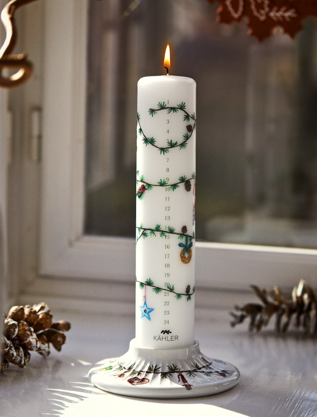 Kähler Design Hammershøi Jul Kalenderkerze 2026 mit Zahlen von 1 bis 24, grünen Tannenzweigen und farbigen Weihnachtsmotiven auf passendem Kerzenhalter.