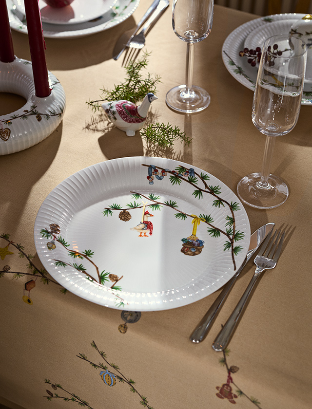 Kähler Design Hammershøi Jul Weihnachtsteller 27 cm aus der 2026 Edition auf festlich gedecktem Weihnachtstisch mit Weihnachtsmotiven, Kerzen, Gläsern und kleiner Weihnachtsgans.