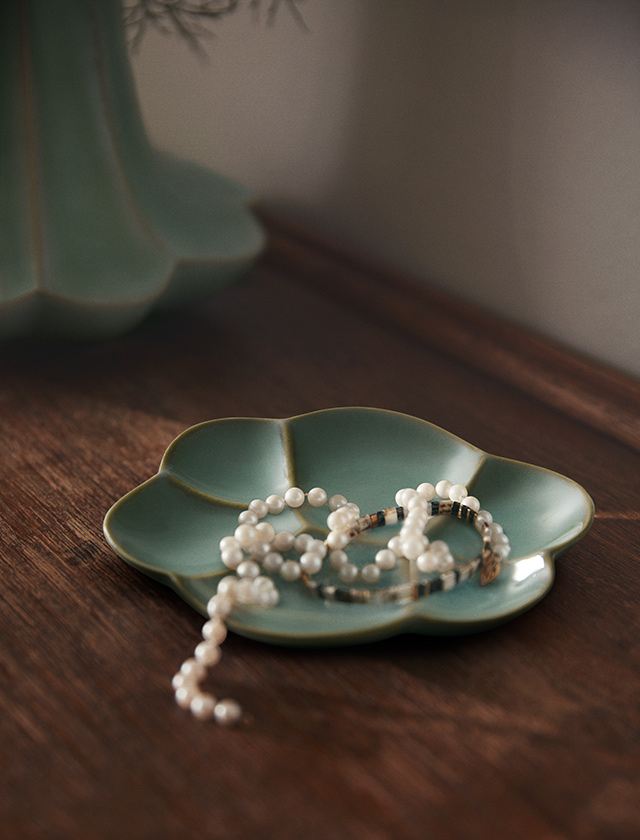 Grüne, blütenförmige Kantarel Schale aus Keramik auf Holztisch mit Perlenkette – stilvolle Ablage für Schmuck.