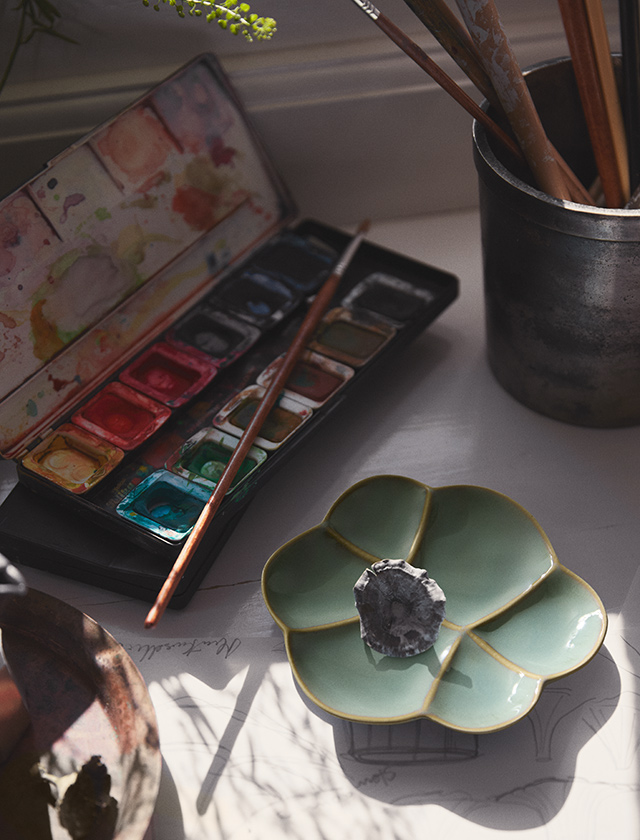 Blütenförmige grüne Kantarel Keramikschale als Ablage, arrangiert am Kreativplatz mit Aquarellpalette, Pinsel und Metallbecher.