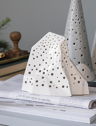 Nobili Mountain Stimmungslicht - Teelichthalter in Schneeweiß von Kähler Design mit einem Nobili Stimmungslicht Kegel in Frostgrau auf einem Sideboard.