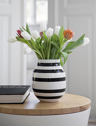 Eine mittelgroße Omaggio Vase mit schwarz-weißen Streifen und einem Strauß von roten und weißen Tulpen. Hier gezeigt auf einem Tisch aus der Unit Serie, ebenfalls von Kähler Design.