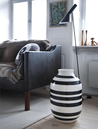 Die ikonische Omaggio Bodenvase von Kähler Design lässt sich wunderbar auch mit weiteren Designklassikern kombinieren. Mit den wundervollen Freemover Kerzenhaltern aus Teakholz, einen Kay Bojesen Affe aus Limbaholz und einer schwarze Arne Jacobsen Stehleuchte setzen Sie weitere stilvolle Akzente.