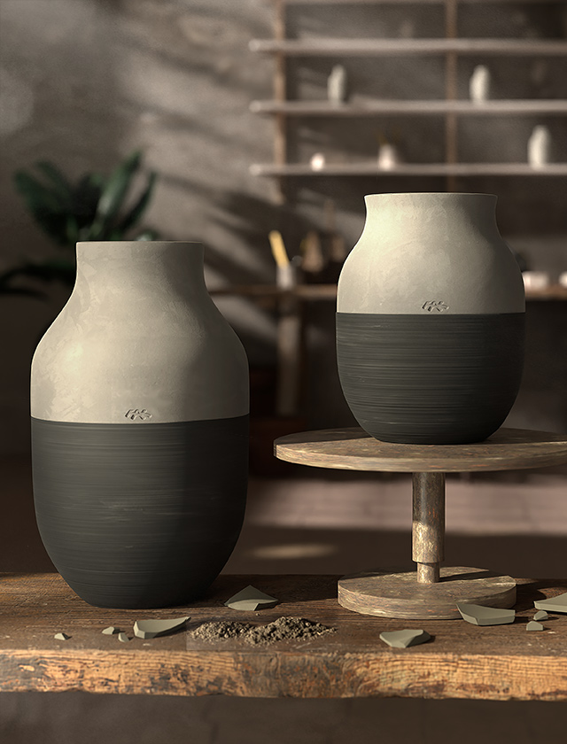 Das Bild zeigt zwei Omaggio Circulare Vasen von Kähler Design. Die eine Vase steht auf dem Boden und die andere ruht auf einer Drehscheibe, typisch für eine Töpferei. Die obere Hälfte beider Vasen präsentiert sich in der natürlichen, unglasierten Tonfarbe, während die untere Hälfte mit einem glatten, dunkelgrauen Glanz überzogen ist. Beide tragen ein kleines, erkennbares Logo, das auf die Markenzugehörigkeit hinweist. Hintergrundelemente deuten auf eine künstlerische Werkstatt hin, mit Regalen, die wahrscheinlich weiteres Keramikzubehör beherbergen. Auf dem Holztisch im Vordergrund sind Tonreste und Scherben verstreut, was auf die handwerkliche Fertigung der Vasen hinweist.