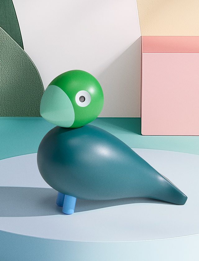Der Kay Bojesen Year Bird 2026 „Birk“ als limitierter Jahresvogel in Nordic-Farben: grüner Kopf, petrolfarbener Körper und blaue Beine – stilvoll inszeniert vor einer modernen, pastellfarbenen Kulisse.