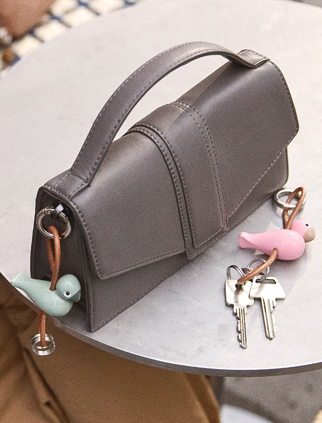 Rosa und mintfarbener Kay Bojesen Vogel Schlüsselanhänger an grauer Ledertasche, neben Schlüsseln auf einem Tisch