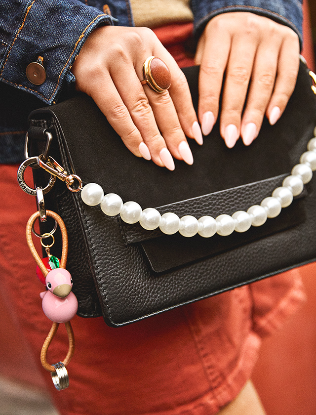 Rosa Kay Bojesen Vogel Schlüsselanhänger an schwarzer Ledertasche mit Perlenhenkel, in der Hand getragen