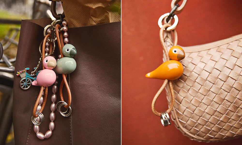 Kay Bojesen Vogel-Schlüsselanhänger in Rosa, Grün und Orange mit Naturlederband und Metallring an Handtasche und Einkaufstasche.