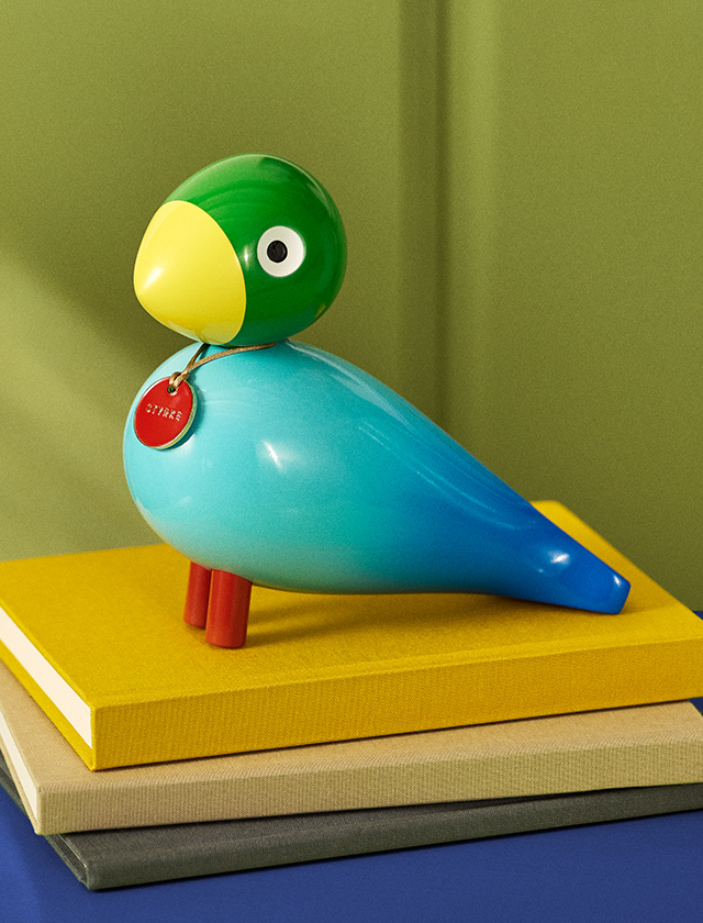 Kay Bojesen Story Bird Power als farbenfrohe Designfigur mit blauem Körper, grünem Kopf, gelbem Schnabel und rotem Power-Anhänger.