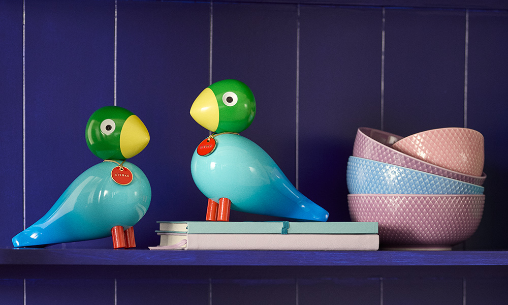 Zwei Kay Bojesen Story Bird Power Singvögel in Grün, Türkis und Blau auf einem Regal neben Büchern und pastellfarbenen Rhombe Schalen von Lyngby Porcelæn.