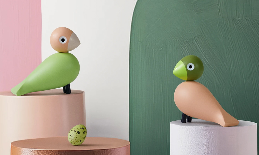 Zwei Kay Bojesen Unzertrennliche aus Holz in Hellgrün und Rosa auf Podesten, daneben ein gesprenkeltes Ei.