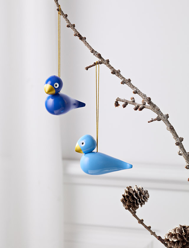Zwei blaue Kay Bojesen Wintervögel hängen an goldfarbenen Schnüren an einem natürlichen Zweig mit Knospen.