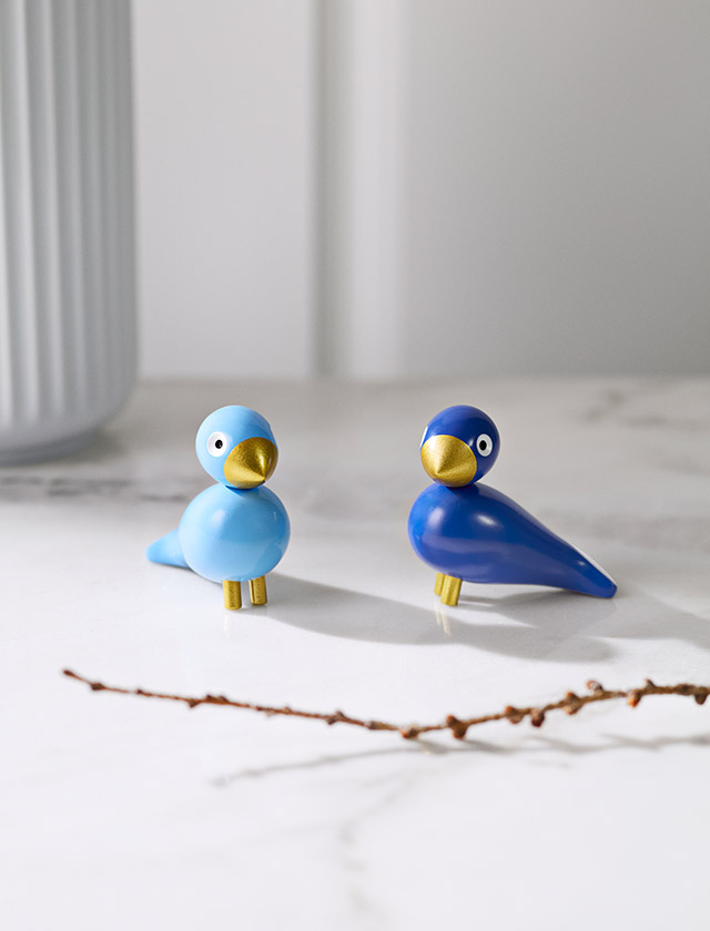 Zwei blaue Kay Bojesen Wintervögel als Paar stehen auf einer hellen Marmortischplatte, dekoriert mit einem Zweig.