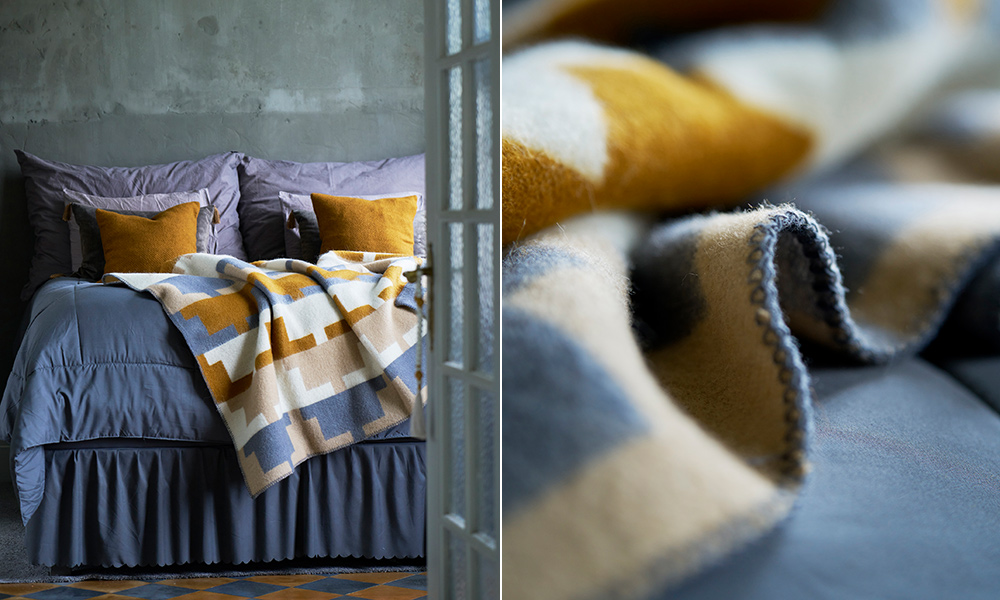 Cancun Wolldecke von Klippan Yllefabrik mit grafischem Muster in Ocker, Beige, Creme und Graublau, dekorativ auf einem Bett mit Gotland Kissen arrangiert.