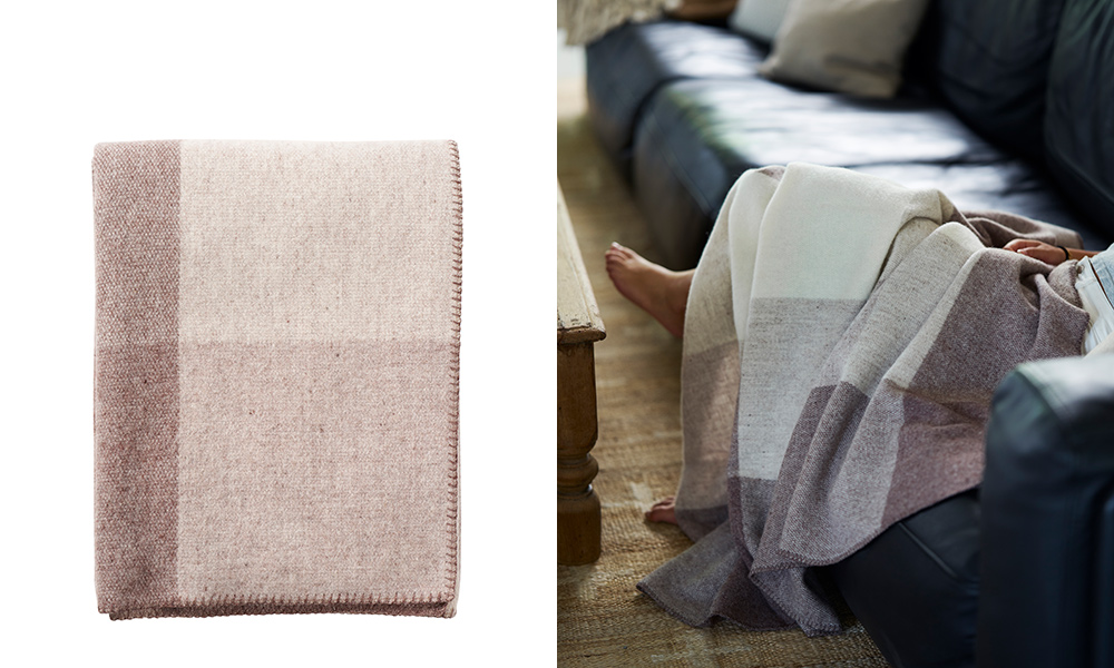 Klippan Field Wolldecke in Beige aus Merino- und Lammwolle, gefaltet und als weiche Wohndecke auf einem dunklen Sofa dargestellt.