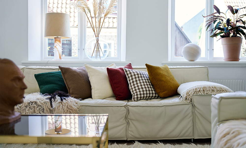 Ein modernes Wohnzimmer mit heller Ledercouch, dekoriert mit verschiedenen Sofakissen von Klippan Yllefabrik. Die Kissenhüllen aus Gotlandwolle und Bouclé-Wolle setzen stilvolle Akzente in natürlichen und warmen Farbtönen. Sie verbinden skandinavisches Design mit gemütlicher Wohnatmosphäre und sind die perfekte Ergänzung zu Wolldecken oder als edle Deko für Sofa und Sessel.