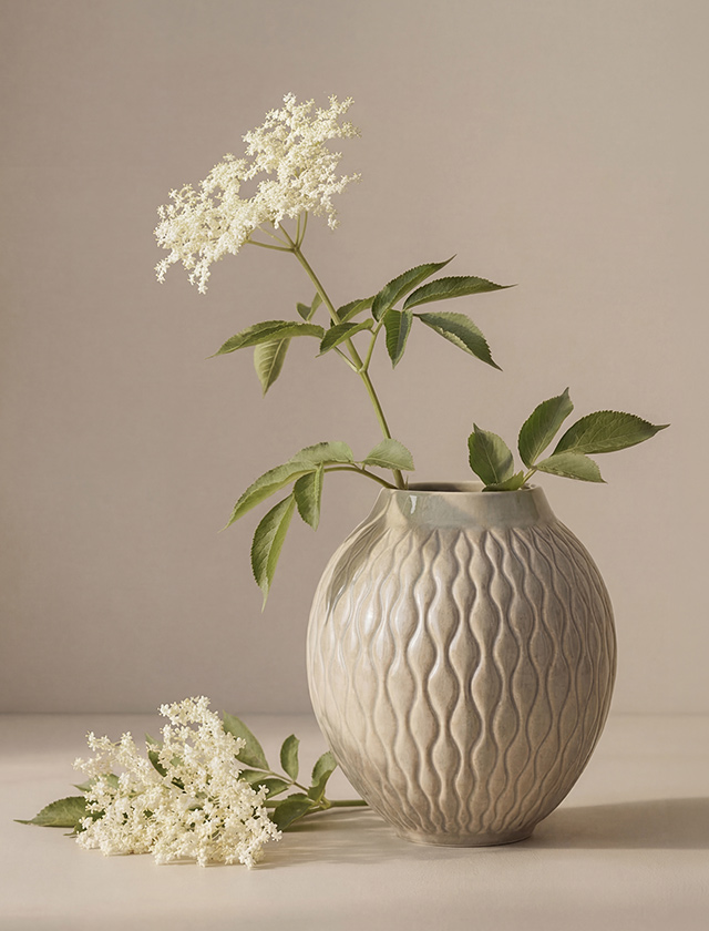 Beige Knabstrup Solum Vase aus Keramik mit organischer Wellenstruktur, dekoriert mit weißen Blütenzweigen in ruhiger skandinavischer Wohnatmosphäre.