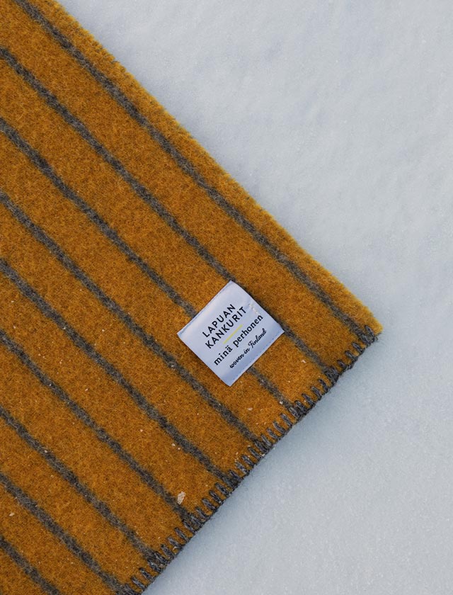 Jedes Detail erzählt eine Geschichte: Das gewebte Label der Aurora-Decke steht für Authentizität, Qualität und nordische Herkunft. Mit viel Liebe zum Handwerk gefertigt, bringt sie die Handschrift von Milla Pettersson in jedes Zuhause. Die Farben – ein Spiel aus wärmendem Orange und reduziertem Grau – symbolisieren moderne Naturverbundenheit.