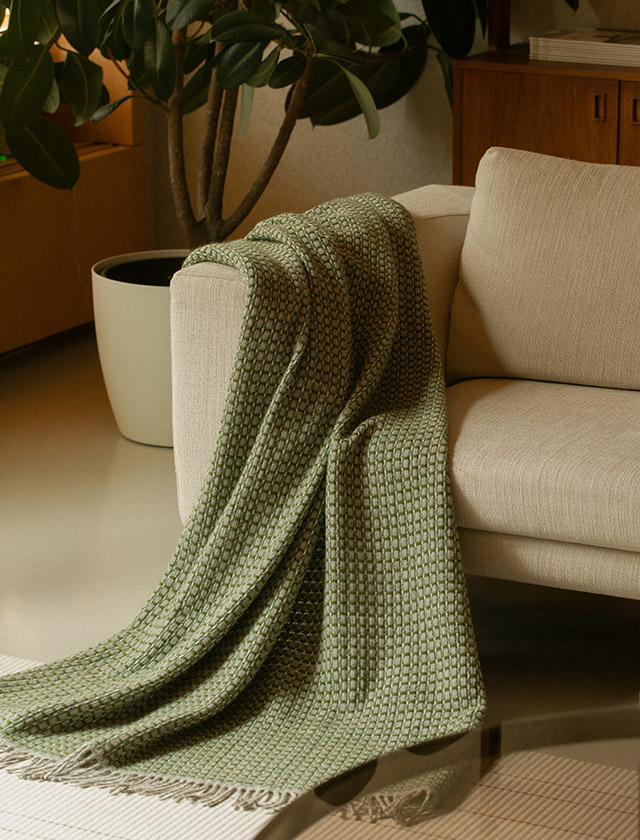 Havas Wolldecken von Lapuan Kankurit aus 100 % Wolle. Weiche finnische Finnschafwolle mit charakteristischem geometrischem Webmuster. Die Decke in der Farbe Olive wurde elegant über ein Sofa drapiert und setzt einen stilvollen skandinavischen Akzent im Wohnraum.