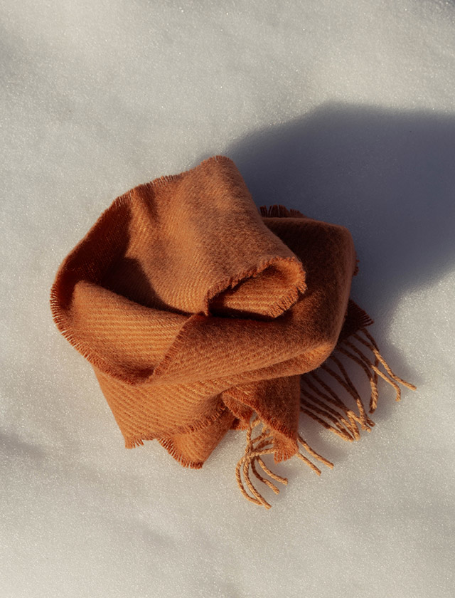 Der ILO Schal von Lapuan Kankurit aus Finnland zeigt die warme, weiche Ausstrahlung hochwertiger Wolle. Das Bild zeigt den Schal locker auf Schnee arrangiert in Cinnamon. Die natürlichen Farben und die feine Webstruktur unterstreichen das nordische Design von Lapuan Kankurit.