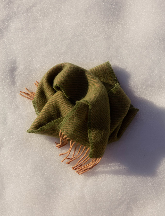 Der ILO Schal von Lapuan Kankurit aus Finnland zeigt die warme, weiche Ausstrahlung hochwertiger Wolle. Das Bild zeigt den Schal locker auf Schnee arrangiert in Powder-Olive. Die natürlichen Farben und die feine Webstruktur unterstreichen das nordische Design von Lapuan Kankurit.