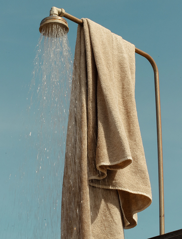 Das Duschtuch Kivi von Lapuan Kankurit aus reinem Leinen in der Farbe White Linen – gezeigt, wie es an einer Außendusche hängt.