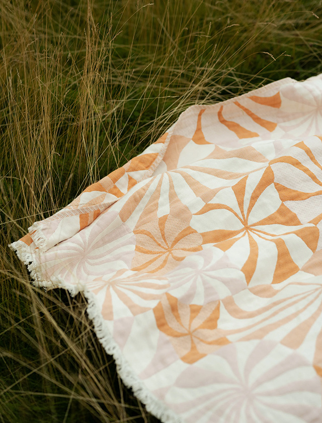 LOISTE Decke von Lapuan Kankurit mit grafischem Blütenmuster in Orange, Rosé und Naturtönen, aus Bio-Baumwolle und Merinowolle, Design Rita Vaali.