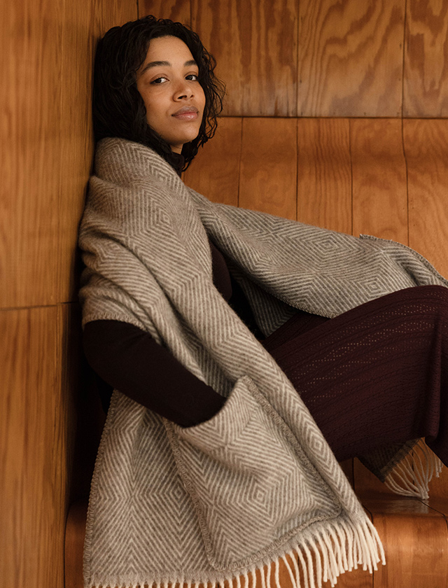 Maria Pocket Shawl von Lapuan Kankurit in Grau-Weiß mit geometrischem Webmuster, Fransen und praktischen Taschen, getragen als wärmender Wollschal.